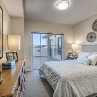 A modern bedroom with neutral decor, featuring a bed, dresser, and lamps.