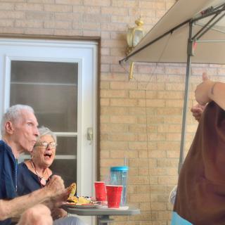 Elderly couple enjoying a meal and laughter outdoors under a canopy.