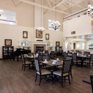 A spacious dining room with elegant decor, featuring multiple tables and chairs, chandeliers, a piano, and a fireplace.