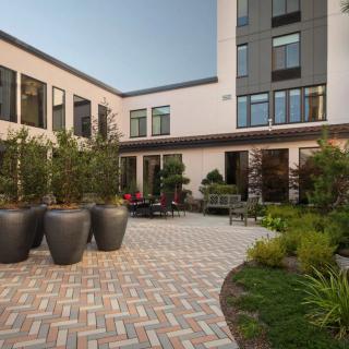 A modern courtyard featuring potted plants and outdoor seating surrounded by contemporary buildings.