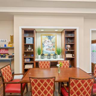 A well-decorated dining area featuring a wooden table with red upholstered chairs, surrounded by bookshelves and artwork on the wall.