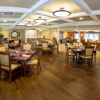 A spacious and elegantly designed dining area with wooden floors, featuring neatly arranged tables and chairs under warm lighting.