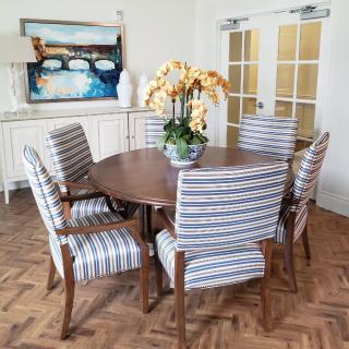 A stylish dining room featuring a wooden table surrounded by striped upholstered chairs, with a floral centerpiece and artwork on the wall.
