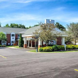 A hotel building with a landscaped entrance and spacious parking area under a clear blue sky.