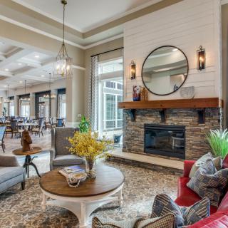 A cozy, modern living room featuring a stone fireplace, stylish furniture, and decorative elements like a mirror and plants.