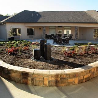 A beautifully landscaped garden with a fountain and outdoor seating area in front of a house.