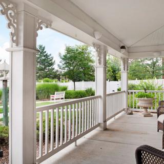 A tranquil porch overlooking a lush garden with comfortable seating and decorative railings.