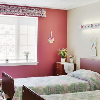 A bright hospital room featuring twin beds, pink walls, and floral decorations.