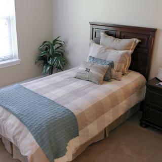 A neatly made single bed with multiple pillows and a bedside table in a well-lit bedroom.