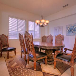A spacious dining room with a large wooden table and elegant chairs, illuminated by a chandelier.