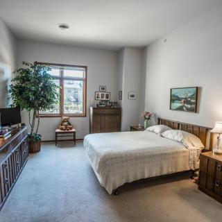 A cozy bedroom featuring a neatly made bed, wooden furniture, and a large window with natural light.