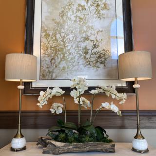 A stylish home interior setup featuring two elegant lamps flanking a floral arrangement, with a large abstract painting in the background.