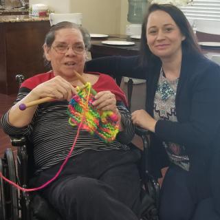 Two people sitting together, one of them knitting with colorful yarn.
