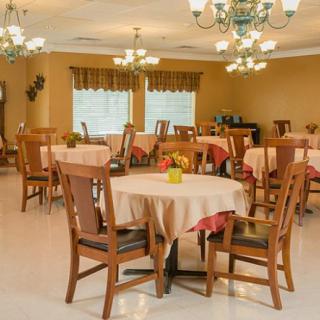 A warmly lit dining room with neatly arranged tables and chairs, featuring chandeliers and large windows.
