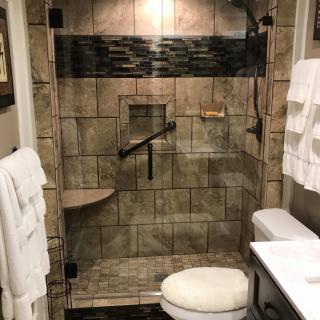 A modern bathroom featuring a tiled shower with glass doors, a grab bar, and neatly arranged towels.