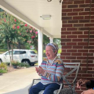 A joyful elderly woman enjoying a sunny day on her porch.