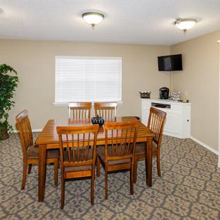 A cozy dining room with a wooden table and chairs, complemented by a patterned carpet and indoor plant.