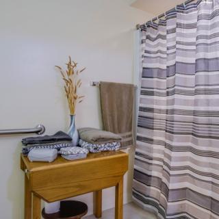 A cozy bathroom with a striped shower curtain, neatly stacked towels, and a wooden table adorned with a vase and decorative plant.