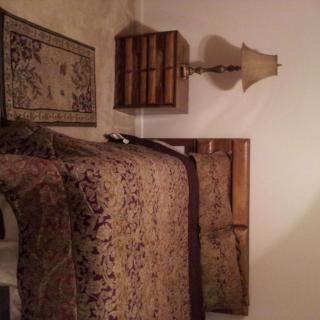 A cozy bedroom with a patterned bedspread, wooden nightstand, and an elegant lamp.