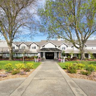 A picturesque view of a large residential building with a landscaped entrance and surrounding trees.