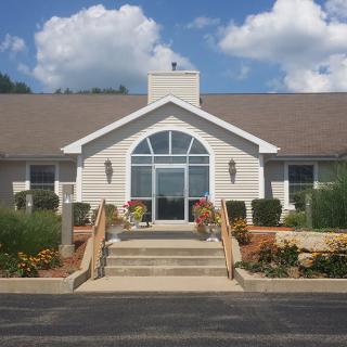 A front view of a building with a large arched window, surrounded by landscaping and set against a cloudy sky.
