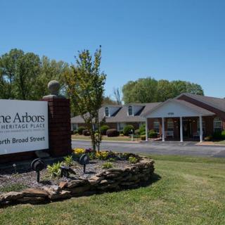 A building with a sign in front, surrounded by landscaping and trees on a sunny day.