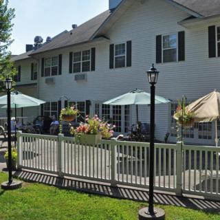 A residential building with a patio area featuring umbrellas and outdoor seating, surrounded by a white fence.