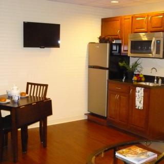 A small kitchen and dining area with wooden cabinets, a table, and a wall-mounted television.