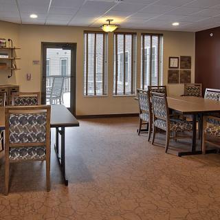 A well-lit dining room with tables and chairs, featuring large windows and modern lighting.