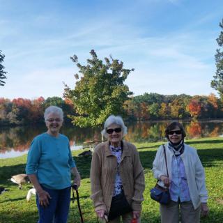 Three seniors enjoying a sunny day by the lake with autumn foliage in the background.