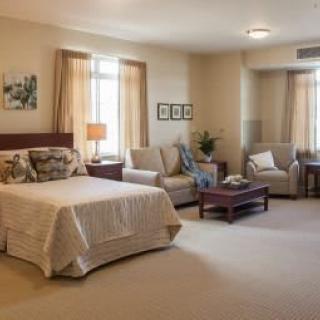 A spacious and elegantly furnished hotel room with a bed, seating area, and soft lighting.