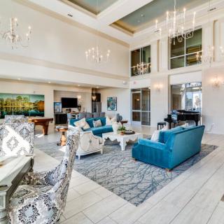 A spacious and elegantly designed living room featuring modern furniture, chandeliers, and large windows.