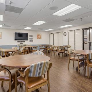 A spacious meeting room with tables, chairs, and a TV mounted on the wall.