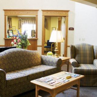 A cozy living room with a sofa, armchair, and coffee table adorned with magazines and a lamp.