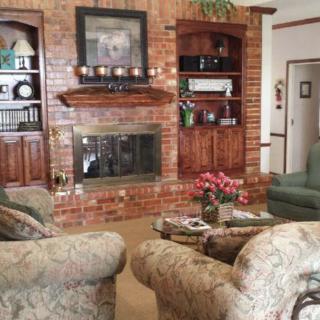 A cozy living room featuring a brick fireplace, comfortable seating, and well-appointed shelving.