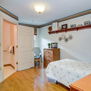 A cozy bedroom featuring a wooden floor, a bed with floral bedding, and decorative items on a wall shelf.