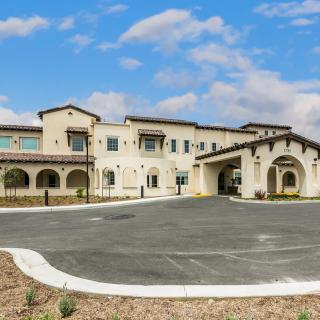 A modern residential building with a spacious driveway and a cloudy sky backdrop.