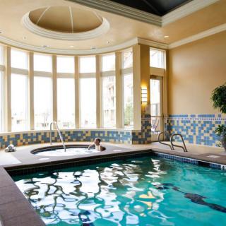 A luxurious indoor swimming pool area with a jacuzzi, surrounded by large windows allowing natural light to illuminate the space.