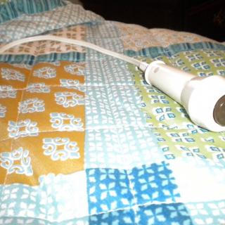 A microphone with a cord resting on a patterned quilt.