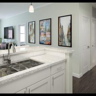 A modern kitchen interior featuring a white countertop and sink, accented by wall art and a pendant light.