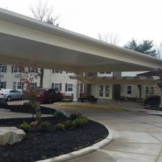 A view of the entrance to a residential building featuring a carport and landscaped surroundings.