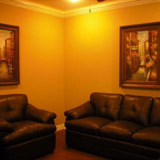 A cozy living room featuring leather sofas and decorative paintings on warm yellow walls.
