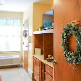 A warm and inviting interior of a room featuring wooden furniture, a decorative wreath, and natural light from the window.