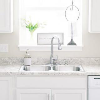 A bright and minimalist kitchen sink area with white cabinets and a decorative plant.