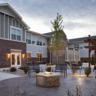 A modern outdoor patio with a fire pit and seating area, set against a backdrop of contemporary architecture and greenery.