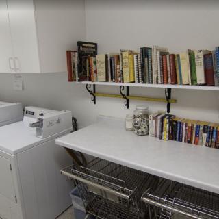 A laundry room with a washing machine, work table, and bookshelves filled with books.