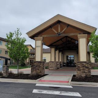 A welcoming entrance to a residential building, featuring a spacious porch and landscaped surroundings.