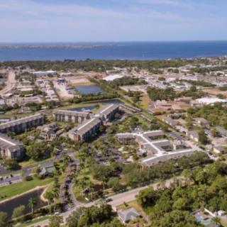 Aerial view of a coastal urban area with buildings, roads, and greenery.