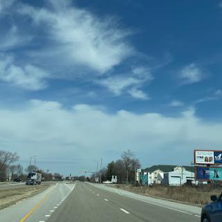 A serene view of a highway stretching into the distance under a clear blue sky with scattered clouds.