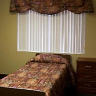 A small bedroom with a single bed and dresser next to the window adorned with curtains.